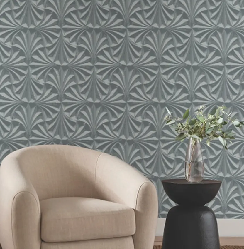 Sillón beige con una mesilla de estilo moderno marrón a su lado y un jarrón con plantas decorando. El fondo es una pared papel pintado creando un relieve en formas de abanico gris.